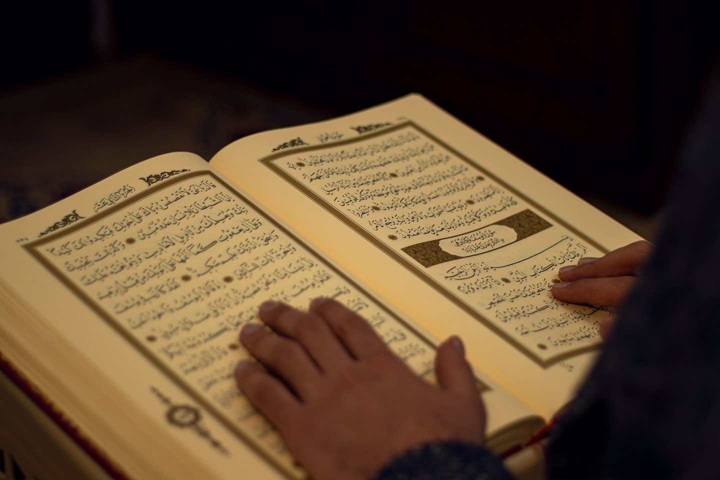 Mani appoggiate su un libro sacro con scrittura araba.